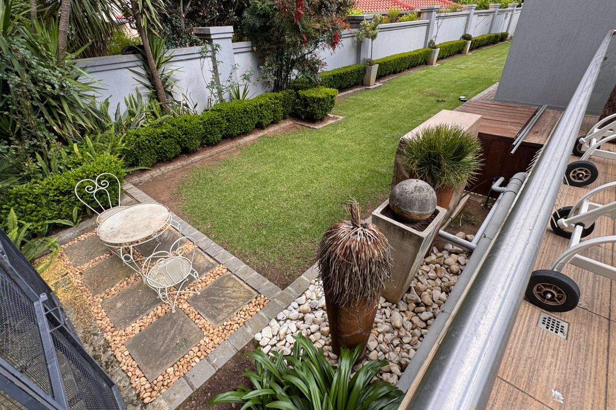A well-maintained rear garden featuring a paved patio area, manicured lawn, and perimeter boundary wall, viewed from an elevated balcony.
