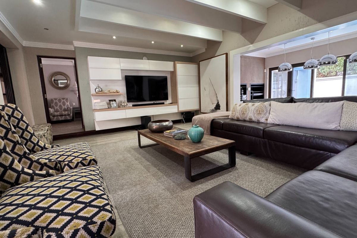 Spacious living room featuring a modern built-in media unit, exposed ceiling beams, recessed lighting, and large sliding glass doors leading to the outdoor area.