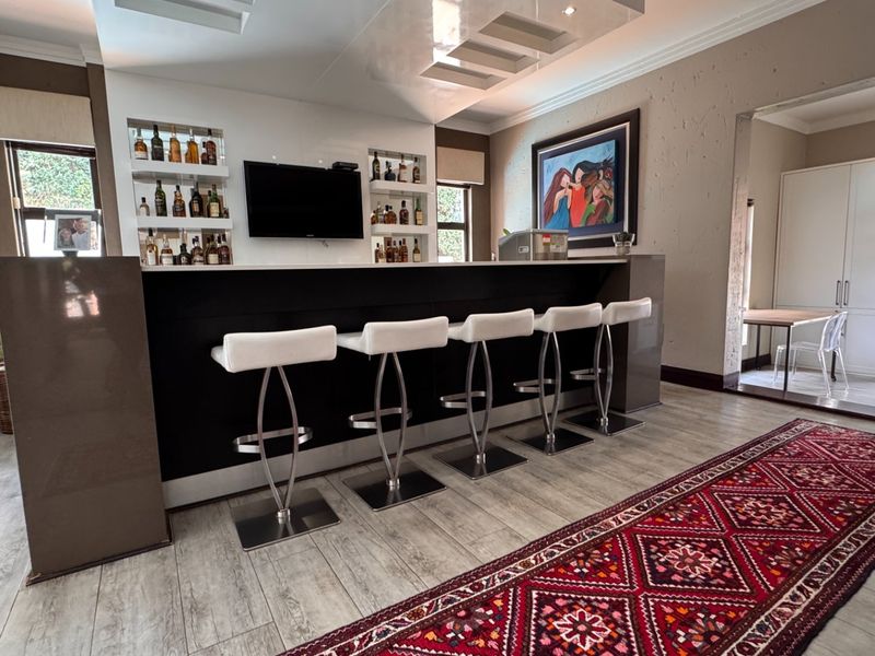 A well-appointed home bar area featuring a sleek built-in counter, recessed display shelving, and modern ceiling lighting, finished with durable tiled flooring.