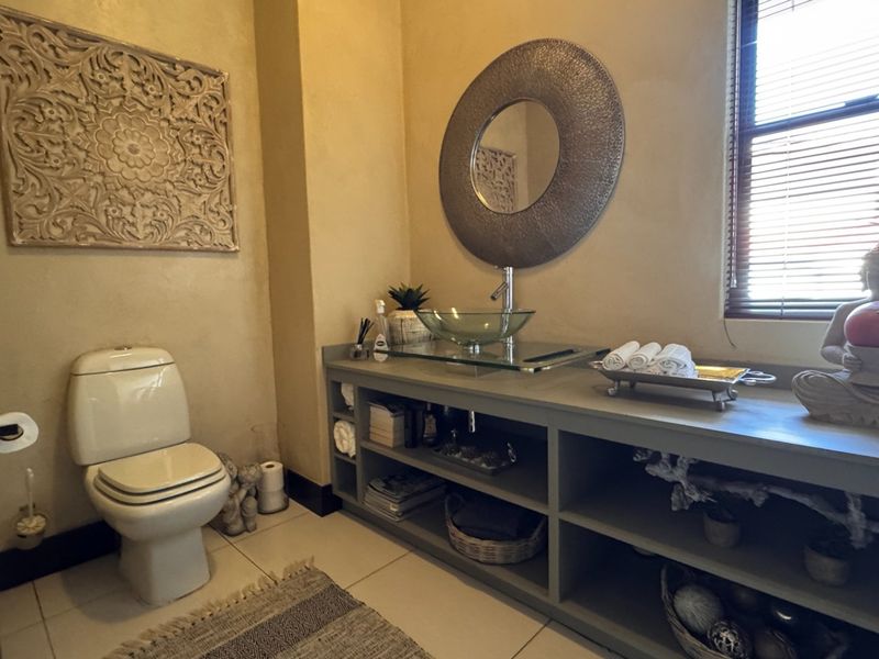 A well-maintained bathroom featuring a custom vanity with open shelving, a glass vessel sink, and a modern toilet.