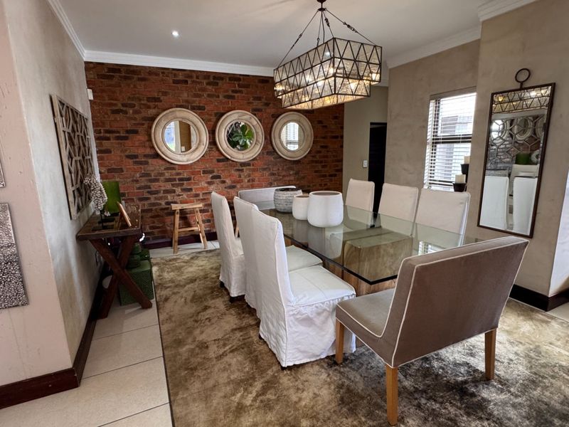Elegant dining room featuring an exposed brick accent wall, modern pendant lighting, and large windows with venetian blinds, creating a warm and inviting atmosphere.