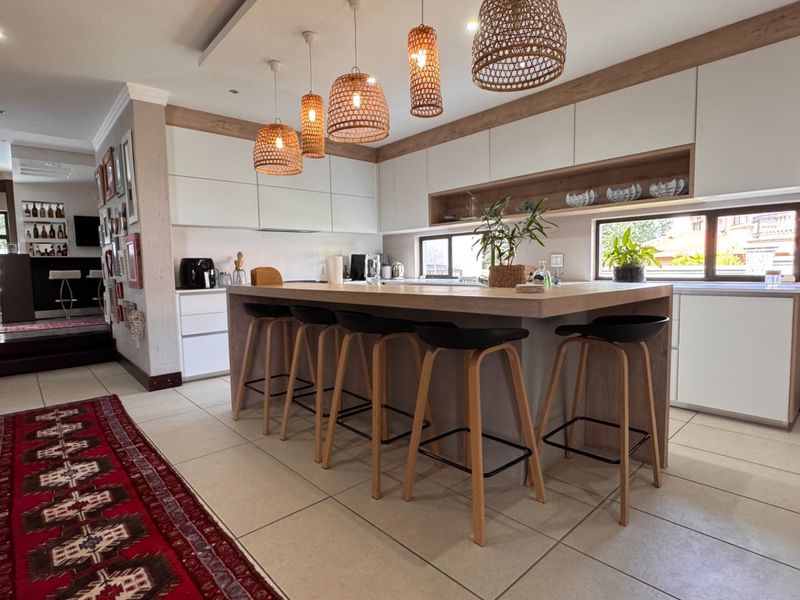 Modern kitchen featuring a large central island with stone countertop, sleek built-in cabinetry, and stylish pendant lighting, complemented by neutral tiled flooring.