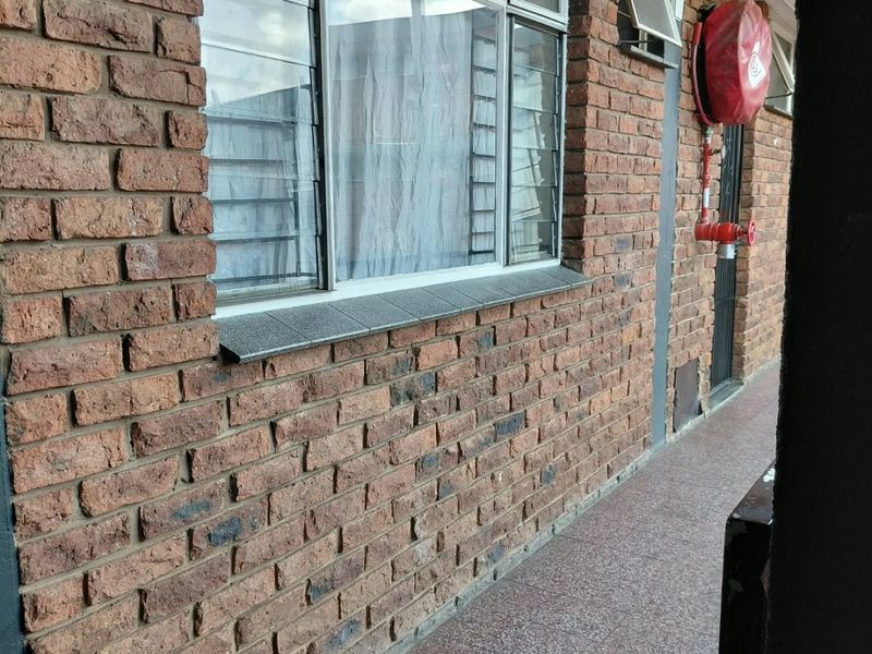 An exterior-facing apartment hallway featuring exposed brick walls, tiled flooring, and a wall-mounted fire hose reel.