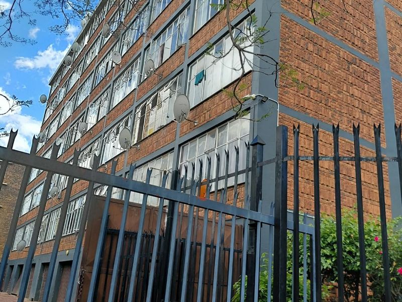 Exterior view of a multi-story apartment building featuring a brick facade, steel-framed windows, and secure perimeter fencing.