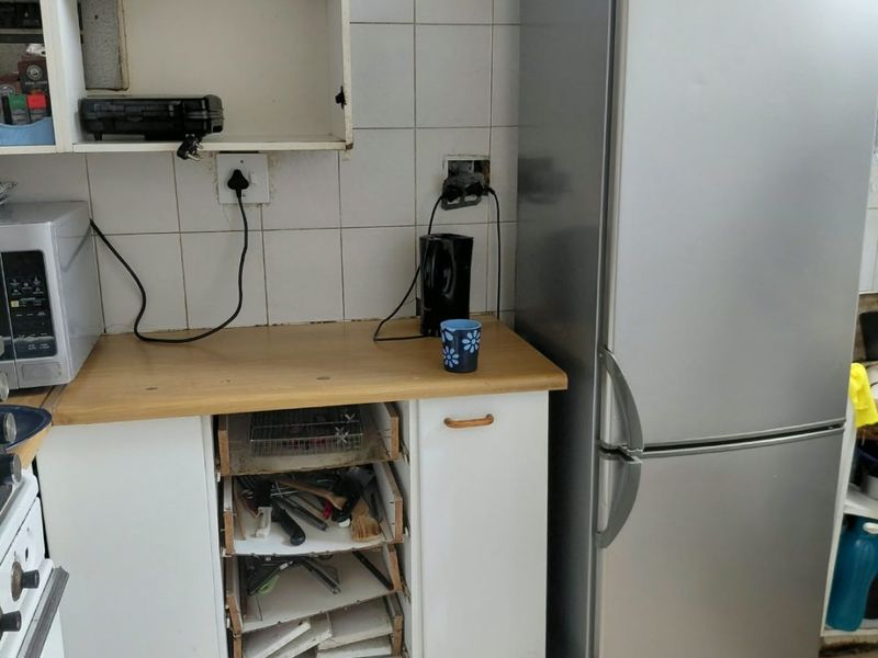 A dated kitchen area featuring tiled splashbacks, laminate countertops, and built-in cabinetry requiring maintenance and cosmetic updates.
