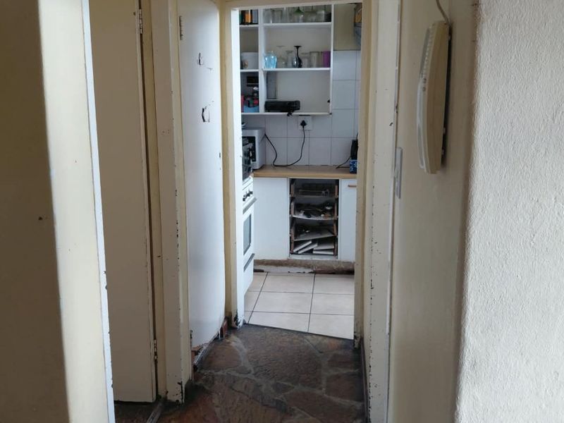 A narrow hallway with stone flooring leading into a kitchen area, featuring built-in storage cupboards and an intercom system.