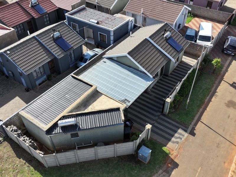 Aerial view of a residential property featuring a tiled roof with solar water heating, a paved driveway, and secure boundary walling.