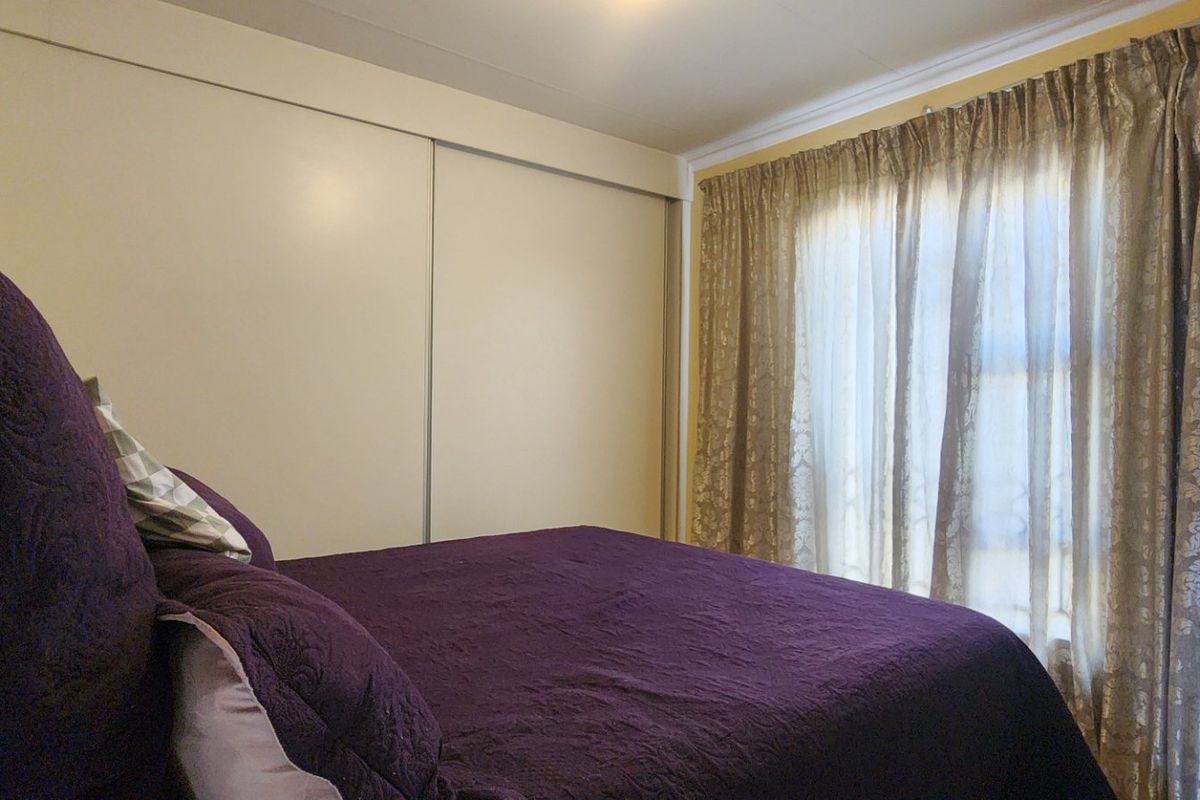 A bedroom featuring a large built-in sliding door wardrobe and window with curtains.