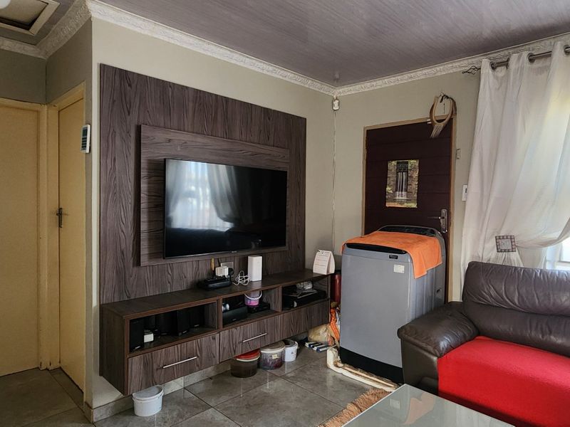 Living room featuring a built-in media unit, tiled flooring, and decorative ceiling coving, providing a functional space with potential for cosmetic updates.
