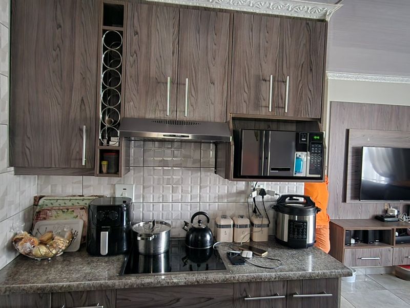 Open-plan kitchen and living area featuring modern wood-grain cabinetry, integrated appliances, tiled backsplash, and a matching built-in media unit.