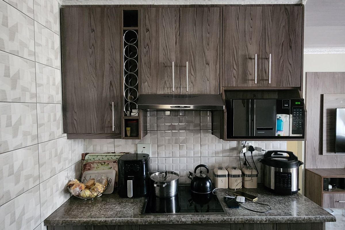 A compact kitchen area featuring modern wood-grain cabinetry, a built-in microwave, extractor fan, and a sleek hob set against a tiled backsplash.