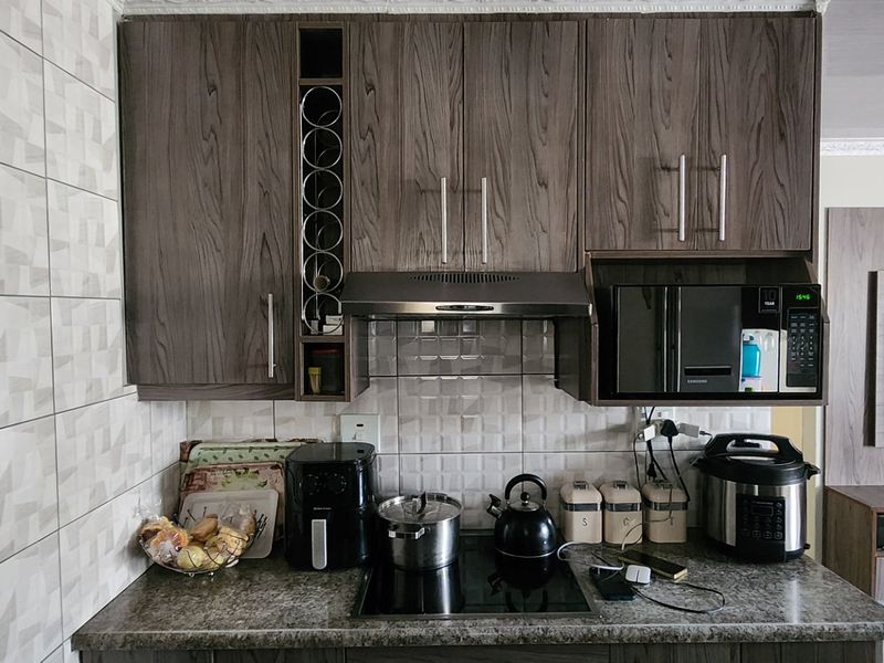 A compact kitchen area featuring modern wood-grain cabinetry, a built-in microwave, extractor fan, and a sleek hob set against a tiled backsplash.