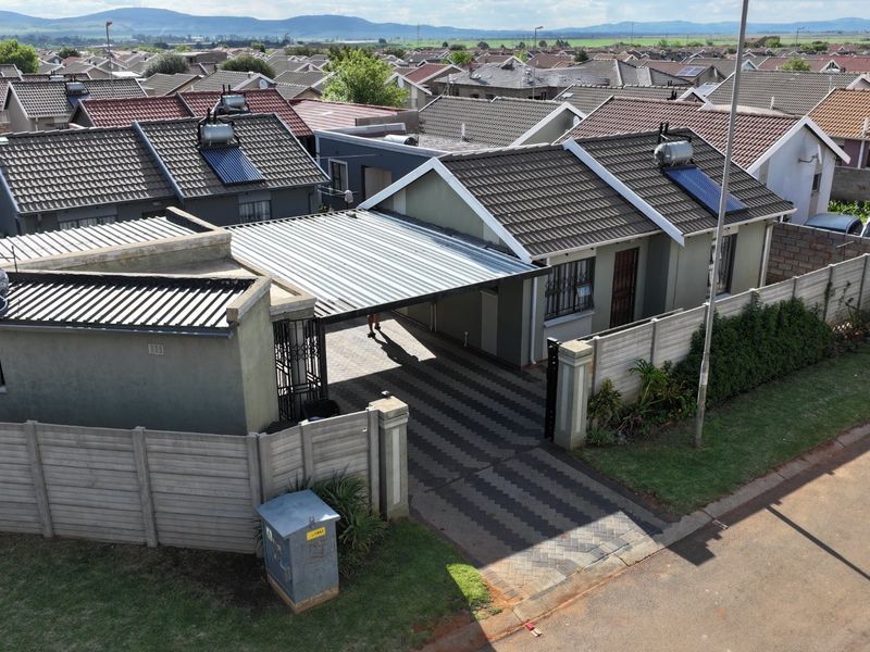 Aerial view of a residential property featuring a paved driveway, carport, and solar water heating system installed on the tiled roof.