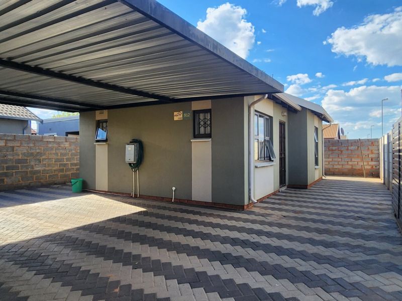 Front exterior view featuring a paved driveway, covered carport, and secure boundary walling.