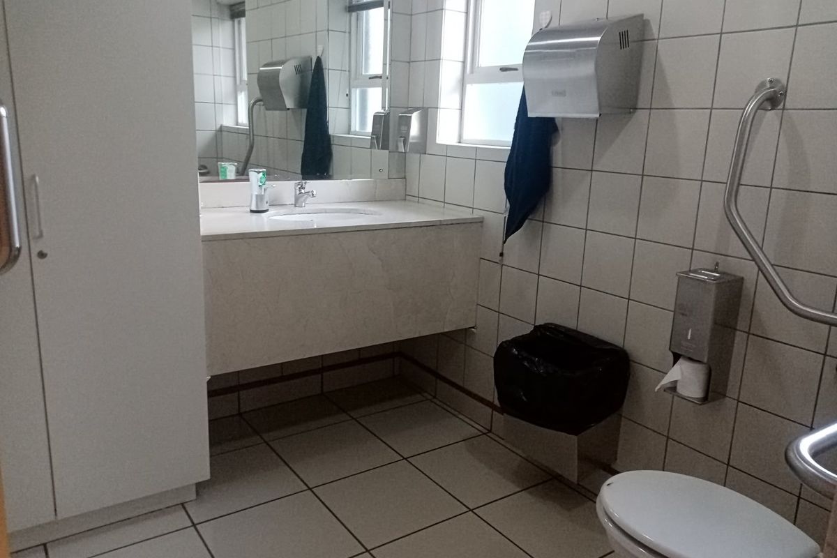 A functional commercial bathroom featuring tiled surfaces, a vanity basin, and accessible grab rails, providing a clean and practical facility.