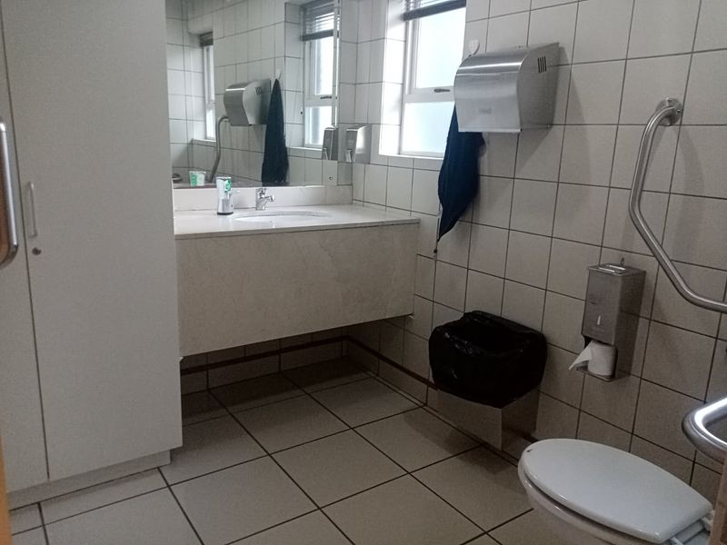 A functional commercial bathroom featuring tiled surfaces, a vanity basin, and accessible grab rails, providing a clean and practical facility.