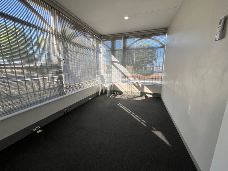 A bright, empty office space featuring large windows with venetian blinds, recessed lighting, wall-mounted air conditioning, and perimeter trunking for convenient power and data access.