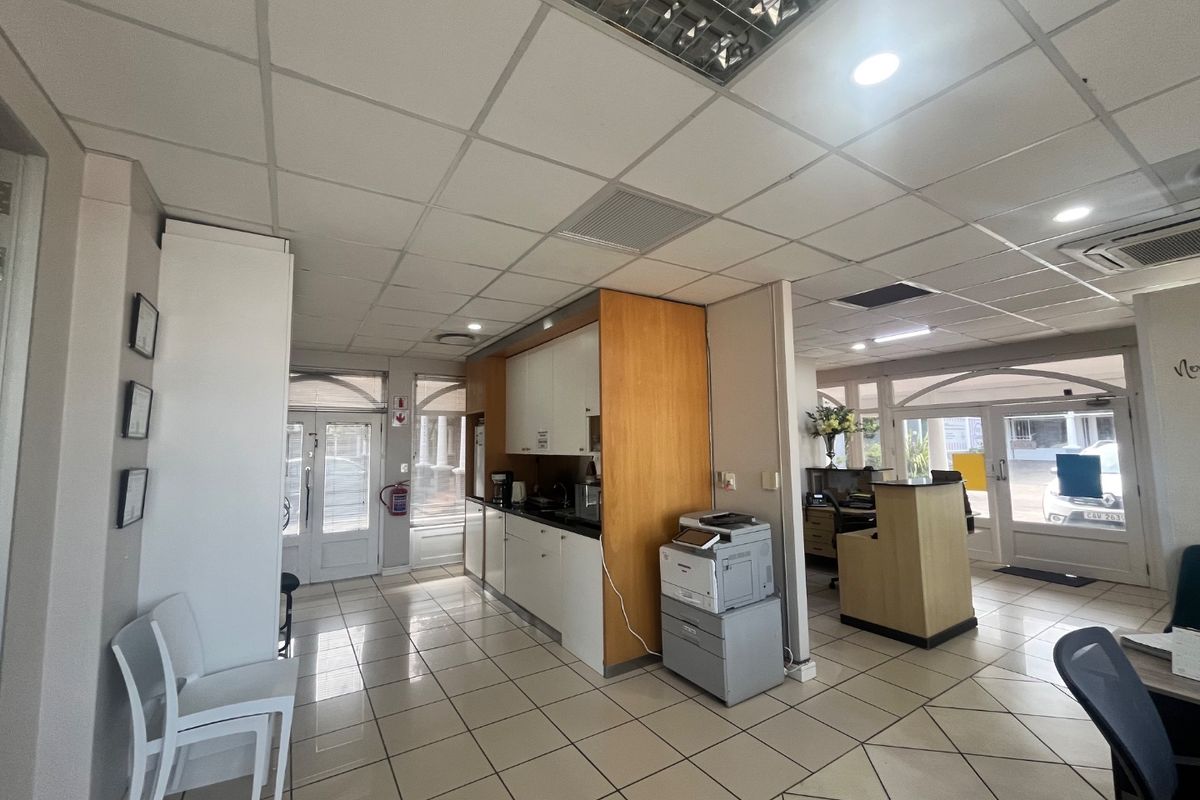 Open-plan commercial office space featuring a kitchenette area, suspended ceiling with recessed lighting, and tiled flooring throughout.