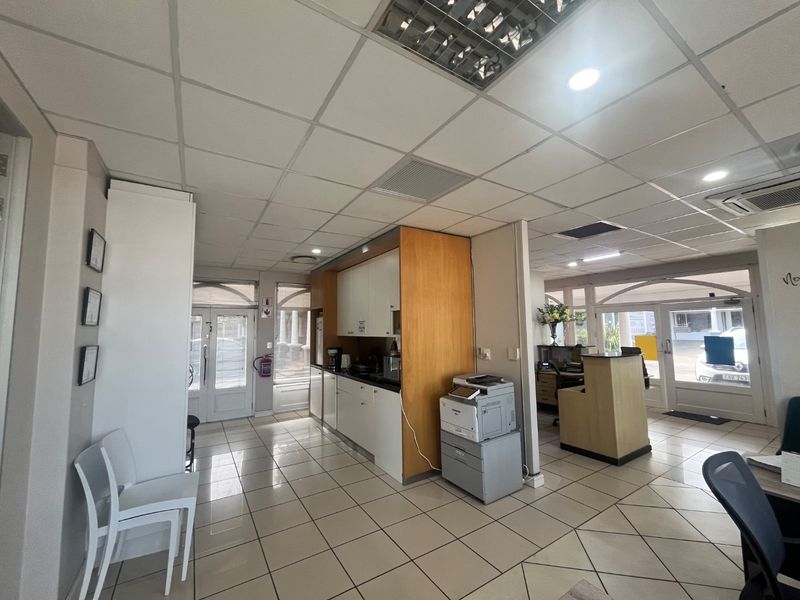 Open-plan commercial office space featuring a kitchenette area, suspended ceiling with recessed lighting, and tiled flooring throughout.