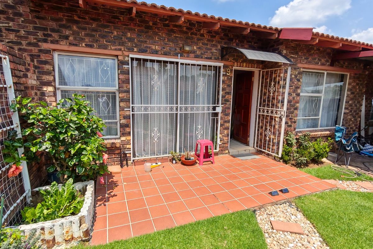 Rear exterior view of a face brick townhouse featuring a tiled patio, security gates, and a built-in planter box.