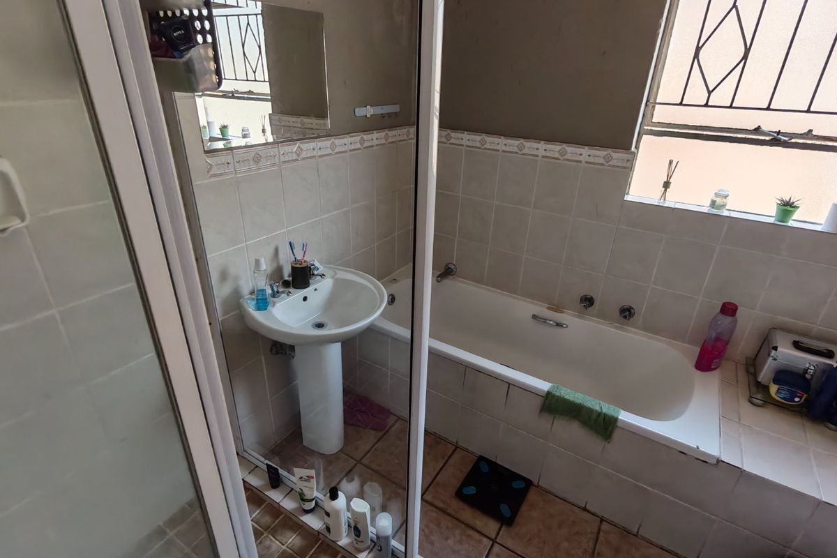 A functional bathroom featuring a pedestal basin, built-in bathtub, and shower enclosure with tiled finishes and security bars on the window.