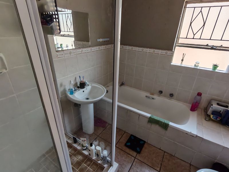 A functional bathroom featuring a pedestal basin, built-in bathtub, and shower enclosure with tiled finishes and security bars on the window.