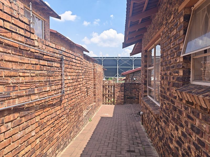 A side exterior walkway featuring face brick walls, paved flooring, and a timber gate, providing access to the rear of the townhouse property.