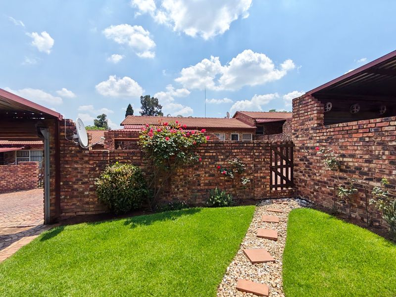 A well-maintained rear garden featuring a manicured lawn, a stone pathway, and face brick boundary walls with a timber gate.