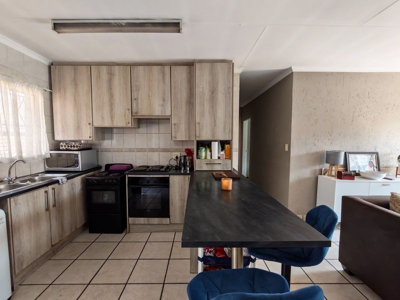 Open-plan kitchen featuring wood-look cabinetry, a black breakfast bar, and tiled flooring, seamlessly connecting to the adjacent living area.
