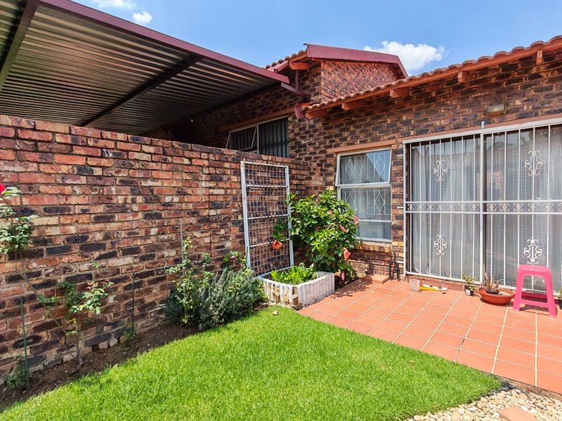 Rear exterior view of the townhouse featuring a face brick facade, a paved patio area, a small lawn, and a covered carport structure.