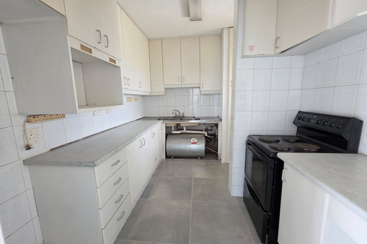 A functional kitchen featuring white cabinetry, laminate countertops, and tiled finishes, currently requiring repairs to the under-sink plumbing and cabinetry enclosure.