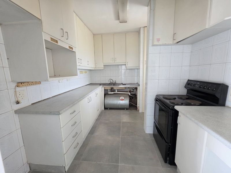 A functional kitchen featuring white cabinetry, laminate countertops, and tiled finishes, currently requiring repairs to the under-sink plumbing and cabinetry enclosure.