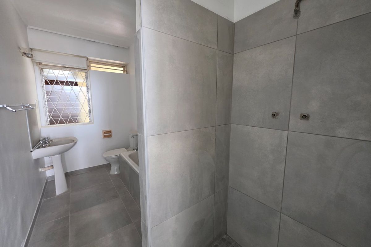 A functional bathroom featuring a pedestal basin, toilet, bathtub, and a tiled shower enclosure with grey wall tiles.