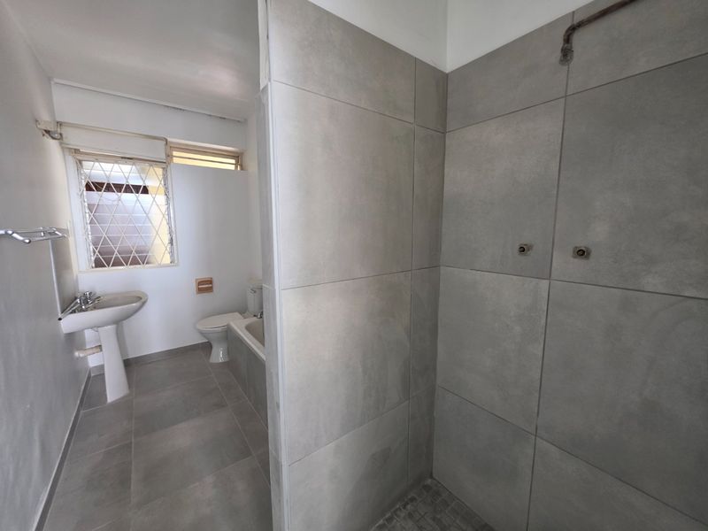 A functional bathroom featuring a pedestal basin, toilet, bathtub, and a tiled shower enclosure with grey wall tiles.