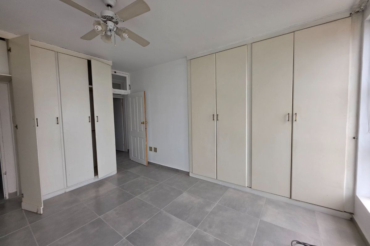A spacious bedroom featuring extensive built-in cupboard storage, a ceiling fan, and neutral tiled flooring throughout.