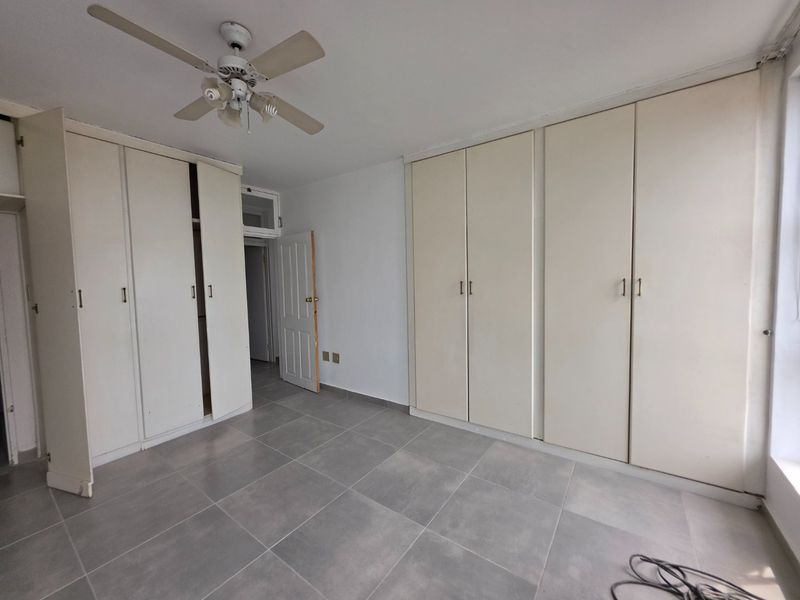 A spacious bedroom featuring extensive built-in cupboard storage, a ceiling fan, and neutral tiled flooring throughout.
