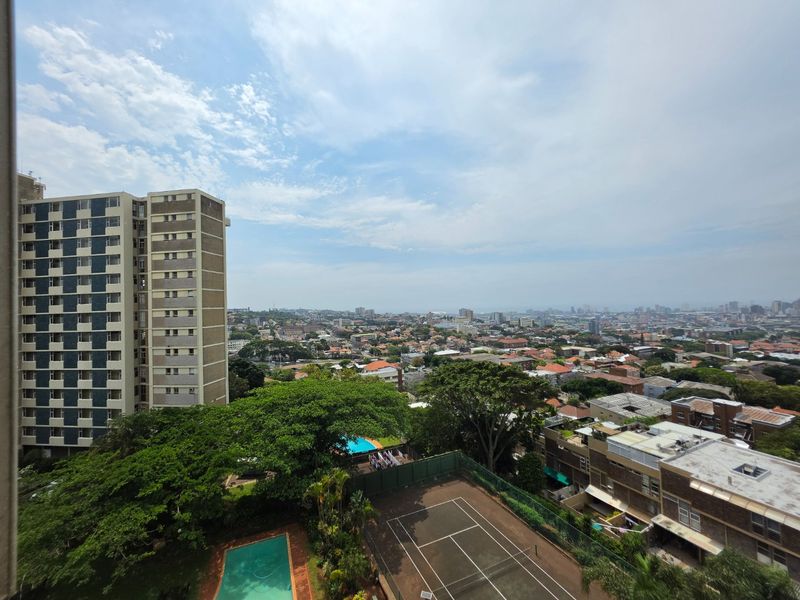 Elevated urban view overlooking the surrounding neighborhood, featuring a communal swimming pool and tennis court within the complex grounds.