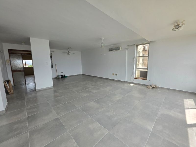 Spacious open-plan living area featuring neutral tiled flooring, ceiling fans, and a wall-mounted air conditioning unit, offering a bright and versatile layout.