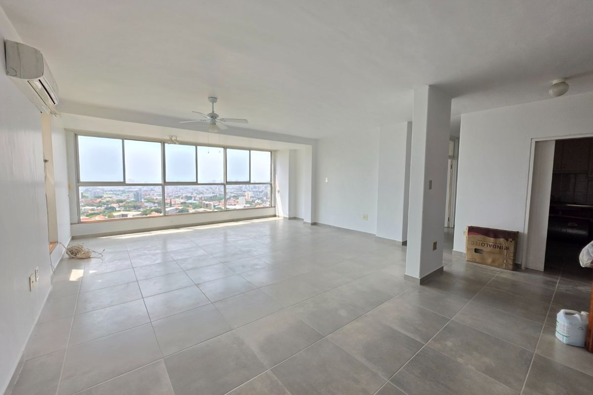 Spacious, sunlit living area featuring large windows with panoramic city views, neutral ceramic tiling, and integrated climate control systems.