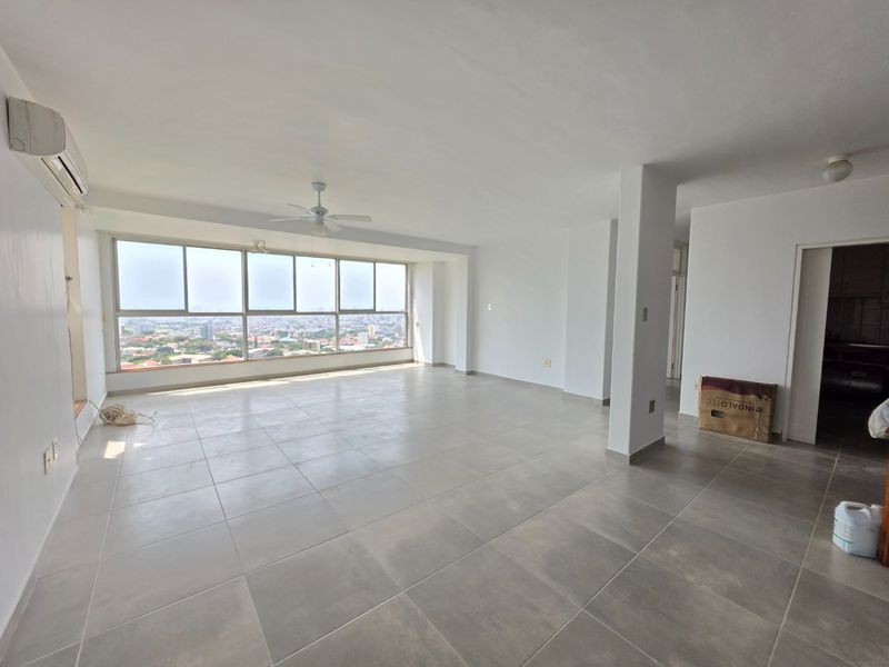 Spacious, sunlit living area featuring large windows with panoramic city views, neutral ceramic tiling, and integrated climate control systems.