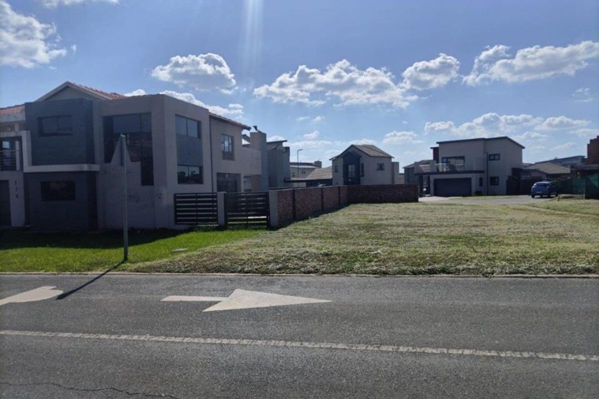 A vacant residential plot situated in a developed estate, featuring a level grass surface and brick boundary walling.
