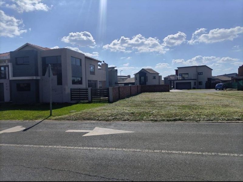 A vacant residential plot situated in a developed estate, featuring a level grass surface and brick boundary walling.