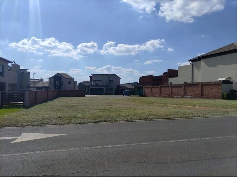 A vacant residential plot situated in a developed neighborhood, featuring established brick boundary walls and direct street access.