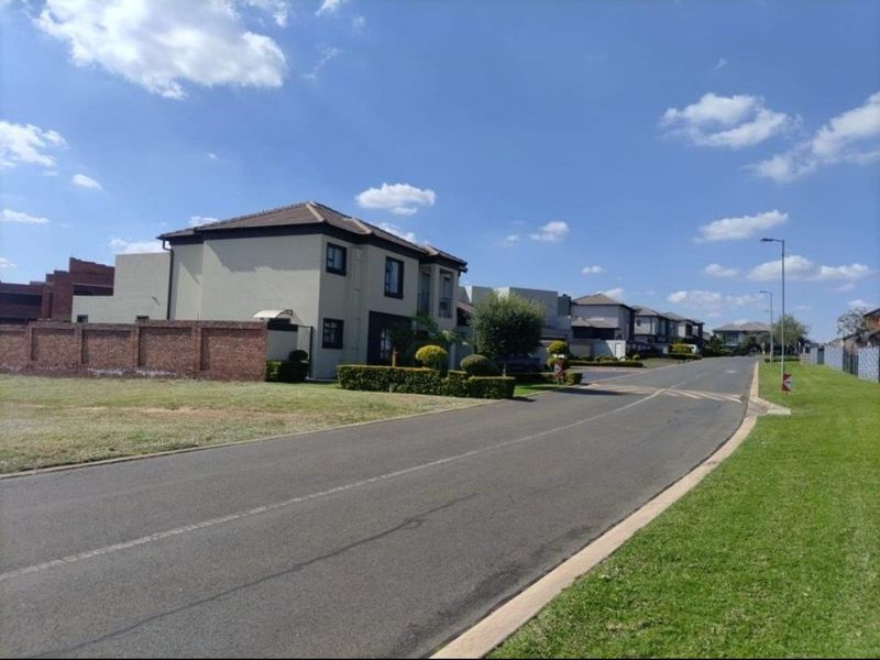 A clear street view of a residential estate featuring paved roads, manicured verges, and established brick boundary walls.