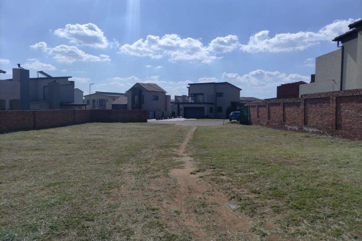 A vacant residential plot featuring a grass lawn and enclosed by brick boundary walls in a developed neighborhood.