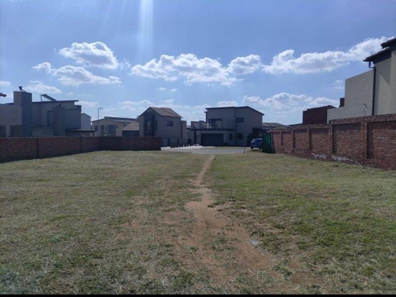 A vacant residential plot featuring a grass lawn and enclosed by brick boundary walls in a developed neighborhood.