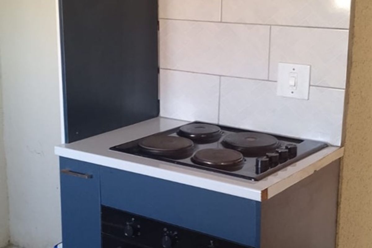 A compact kitchen area featuring modern blue cabinetry, a built-in electric oven and hob, extractor fan, and tiled backsplash.