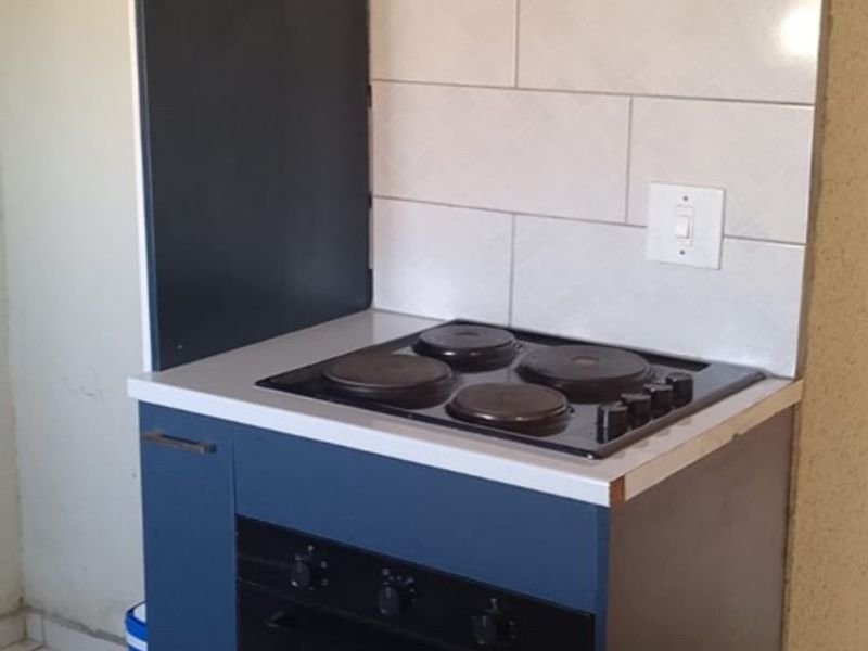 A compact kitchen area featuring modern blue cabinetry, a built-in electric oven and hob, extractor fan, and tiled backsplash.