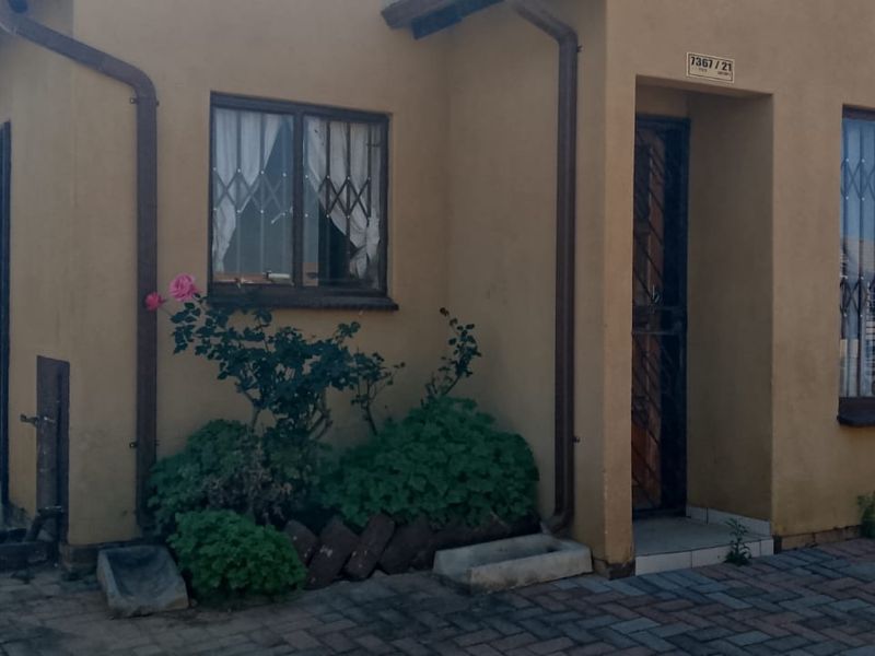 Front elevation of a single-story house featuring paved driveway, security gates, and burglar bars on windows.