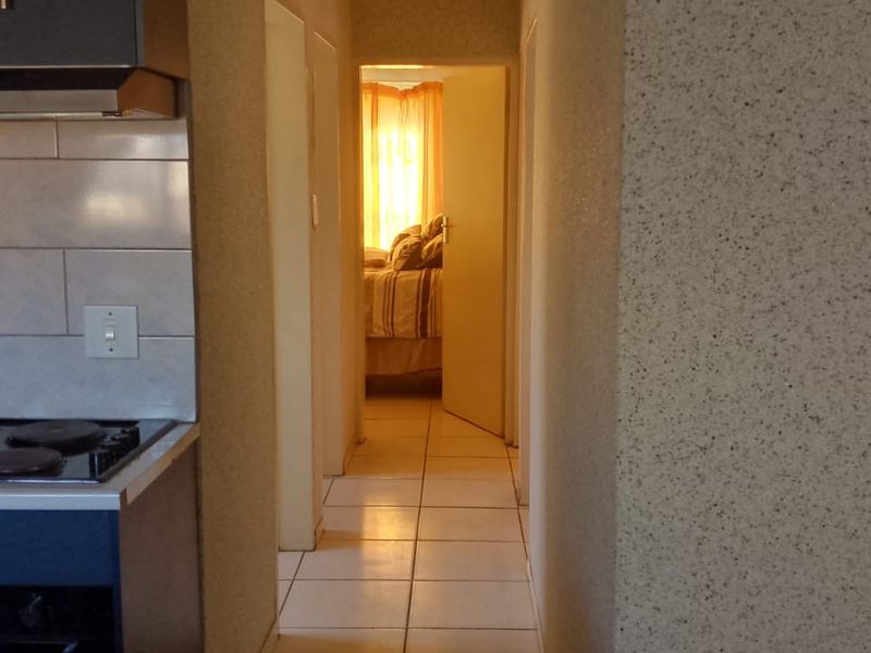 A functional kitchen area featuring built-in cabinetry, a stove with an extractor fan, and tiled flooring, leading into a hallway.
